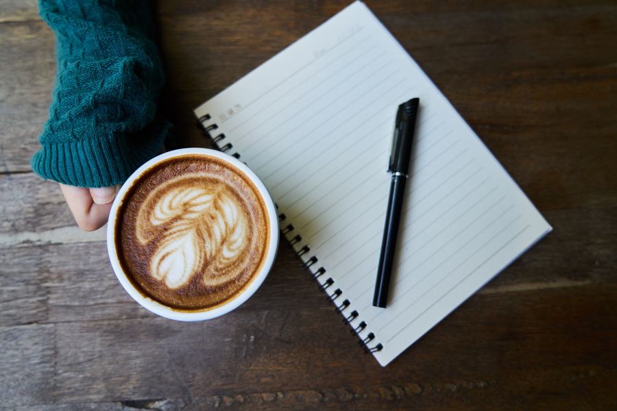 Un quaderno, una penna e un cappuccino su un tavolo di legno. Fotografia d’ispirazione.