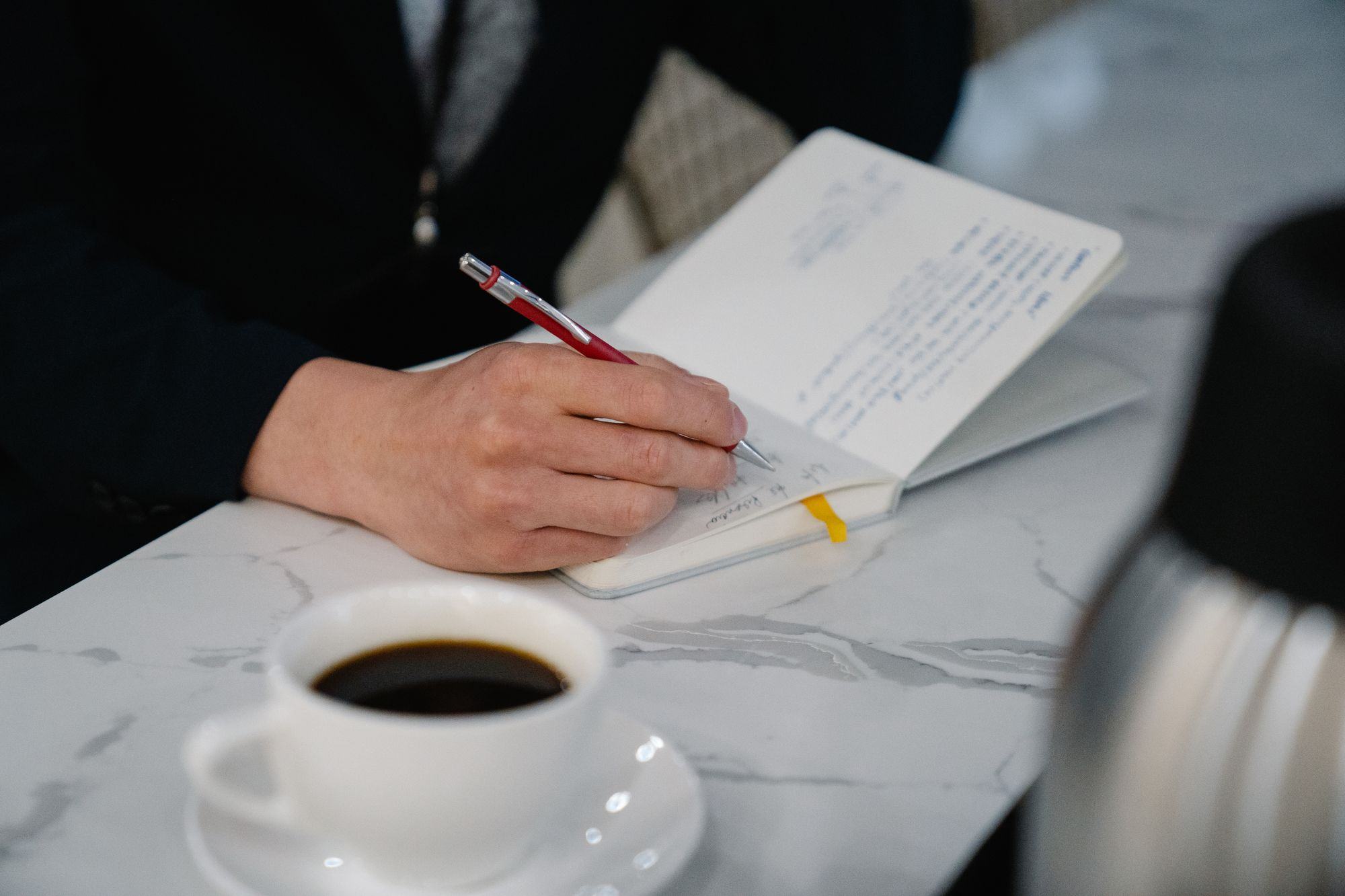 Una persona prende appunti su un taccuino, accanto a un caffè. Fotografia d’ispirazione.