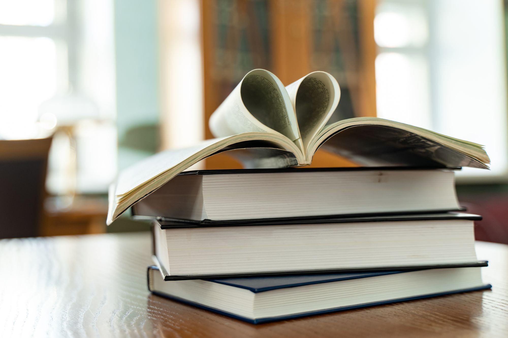 Un libro aperto sopra una pila di libri, su un tavolo di legno. Fotografia d’ispirazione.