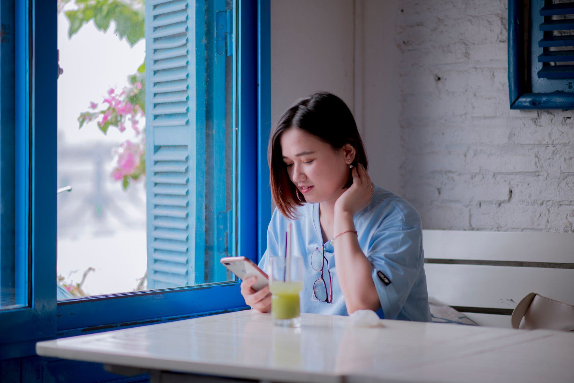 Una ragazza guarda il telefono seduta accanto a una finestra azzurra. Fotografia d’ispirazione.